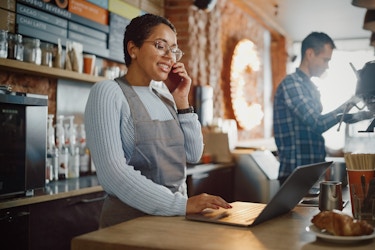  Two people working inside a cafe, one making a coffee and the other on the phone. 