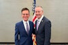 two men in suits standing in front of a flag