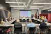 a group of people sitting at a table in a room with a projector screen