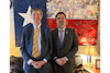 two men in suits standing in front of a flag